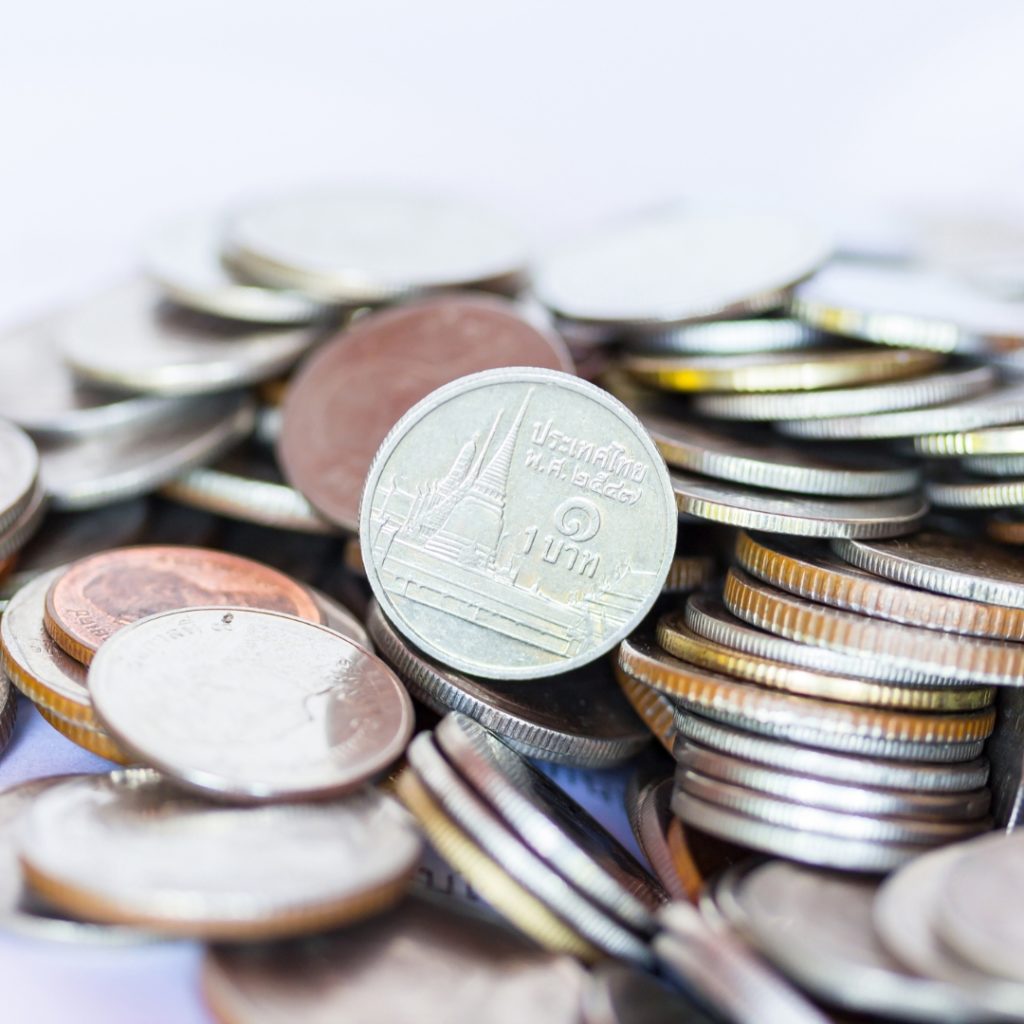 Close-up of a pile of Thai baht coins, a 1 baht coin featuring Wat Arun temple in focus.