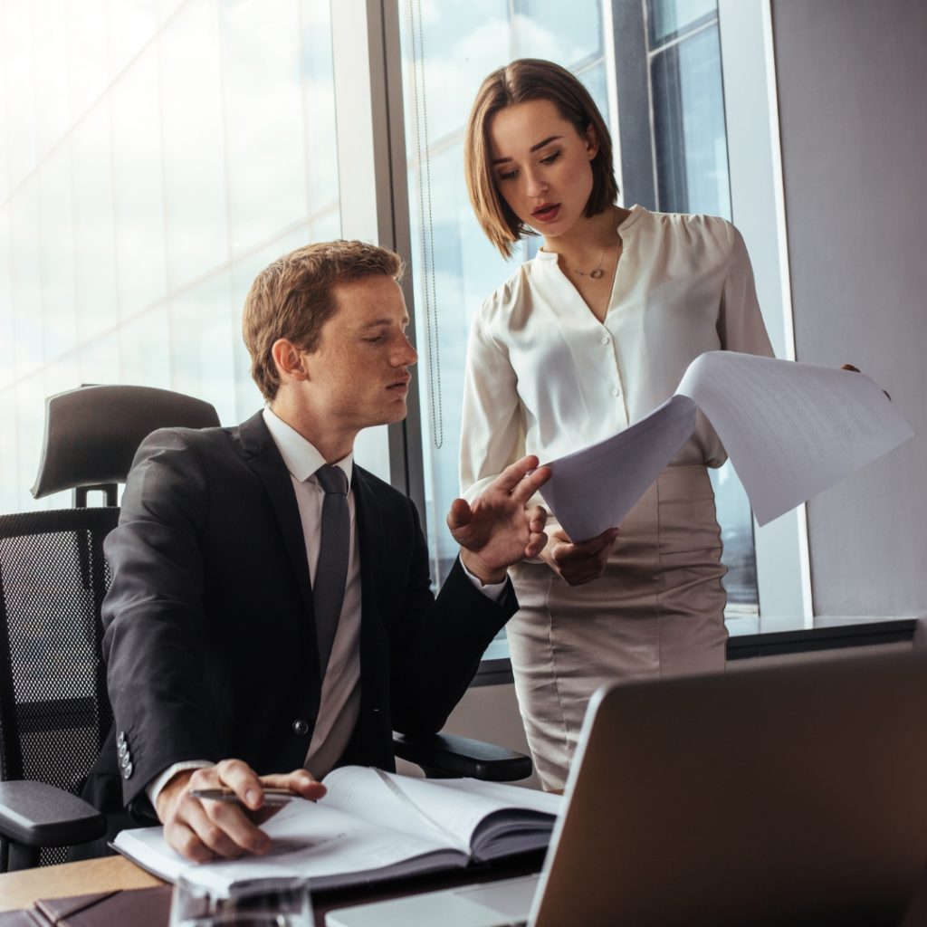 Two business professionals discussing documents in a bright, modern office with large windows.