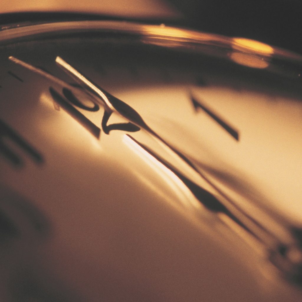 Close-up of an analog clock face with hands pointing near 12 o'clock, bathed in warm, golden light.